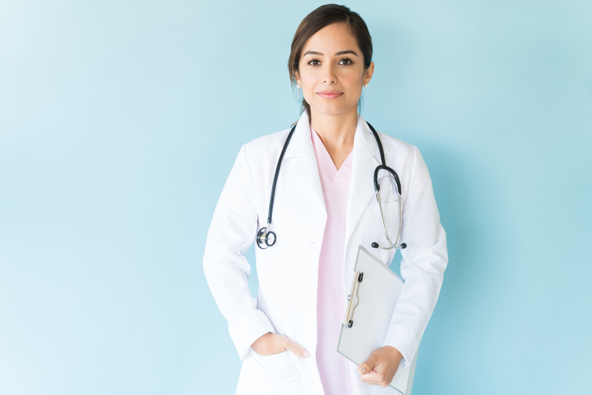 Good looking medical professional with stethoscope and clipboard against plain background